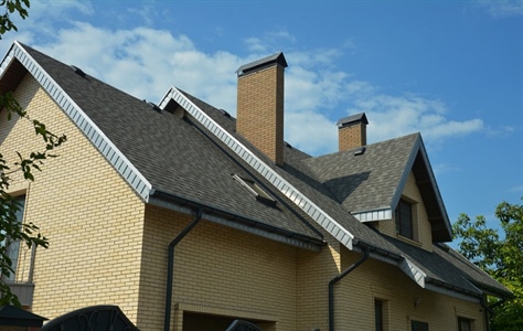 Angle shot of light brown brick home with shingle roofing.